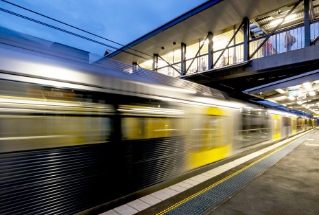 A train moving under the pedestrian access bridge and past the platform