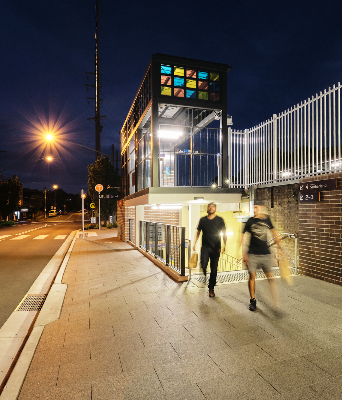 Two men carrying shopping bags exit the Banksia Station underpass at night.