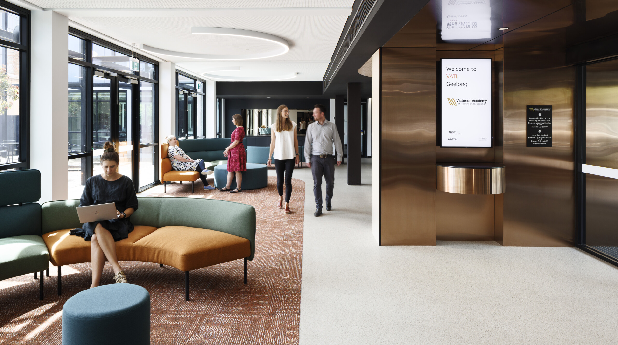 People chatting and working in a guest lounge that has fabric upholstered sofas and brick colour carpet
